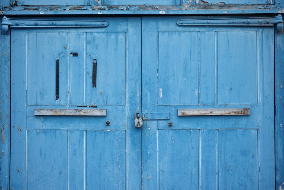 A close-up of rustic blue wooden double doors, securely padlocked, showcasing aged textures.